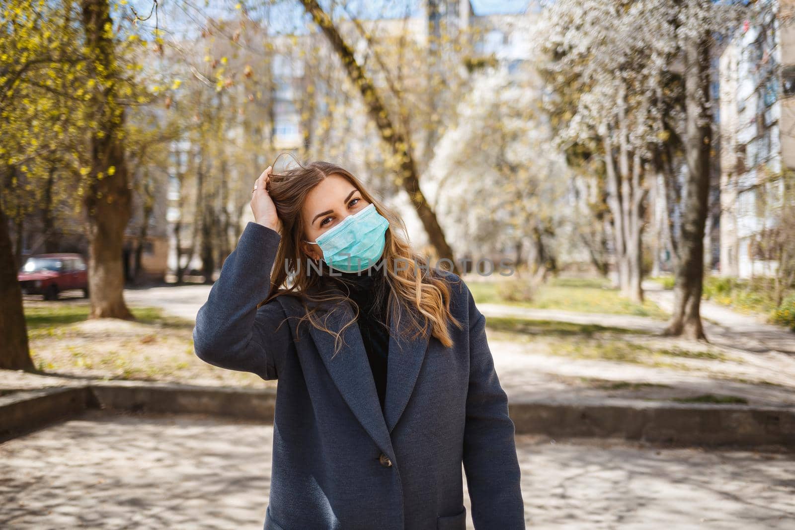 Girl, young woman in a protective sterile medical mask on her face, looking at the camera outdoors, in the spring garden. Air pollution, virus, pandemic coronavirus concept.