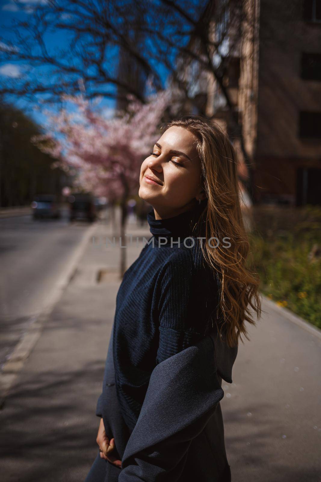 Sakura branches with flowers on a tree on the city streets. Stylish woman girl runs on the street with blooming sakura. Gorgeous fashionable girl outdoors. Sakura tree blossoms.