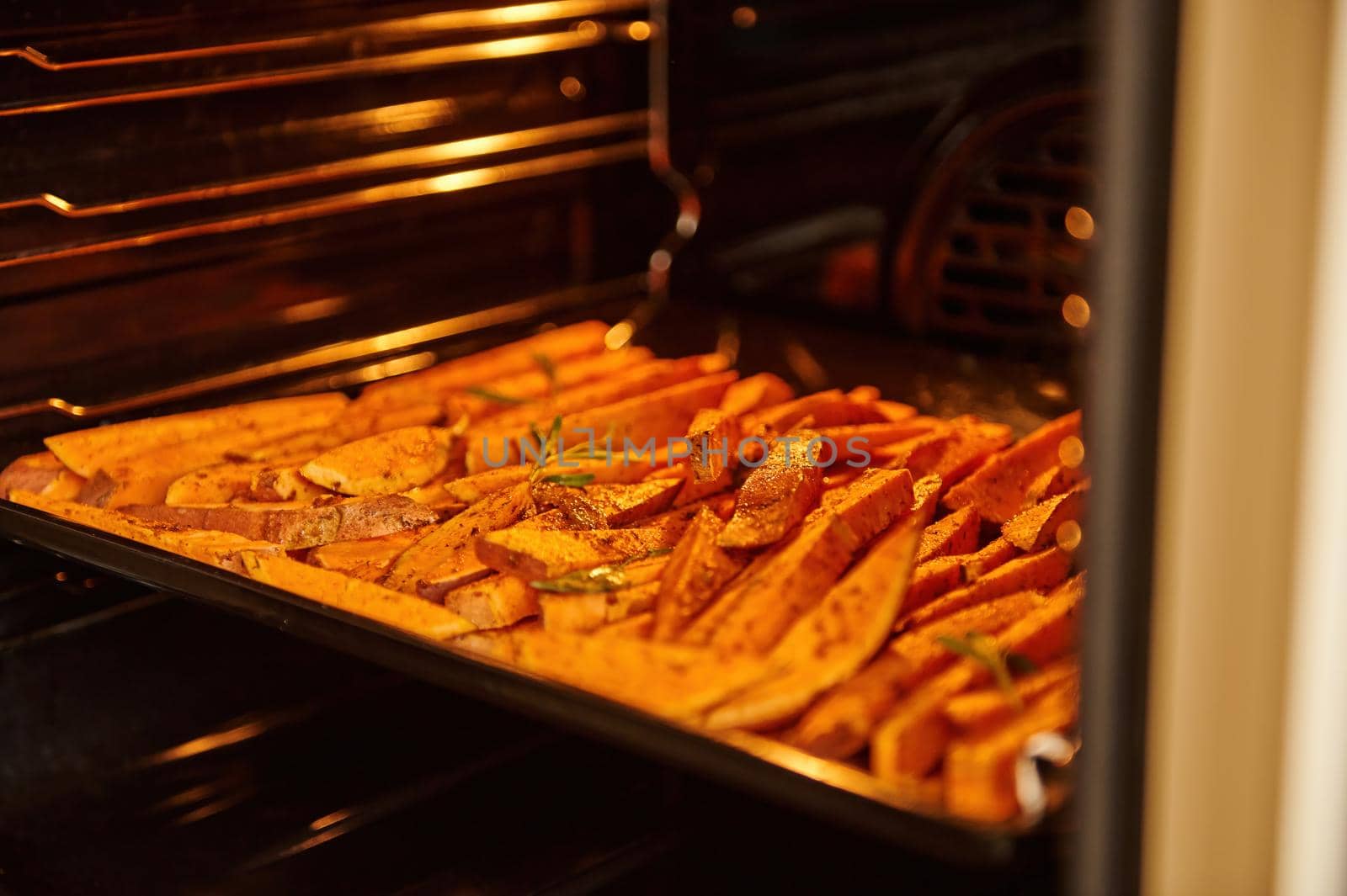 Close-up of sliced sweet potatoes, wedges of batata on a baking sheet, baked and fried with spices and herb in the oven by artgf