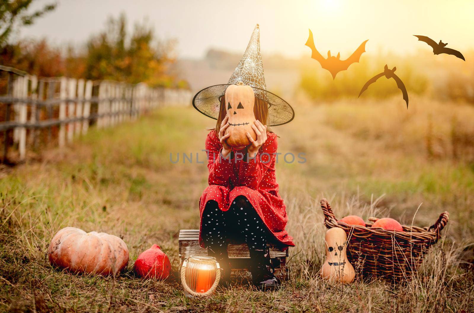 Little girl in halloween costume sitting next to pumpkins while frightening at camera on autumn nature