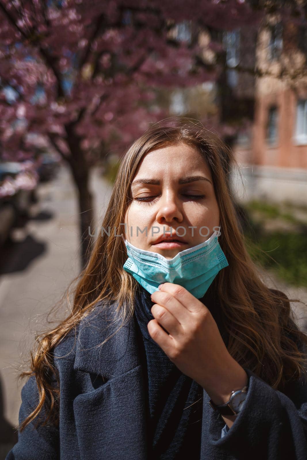 Girl, young woman in a protective sterile medical mask on her face, looking at the camera outdoors, in the spring garden. Air pollution, virus, pandemic coronavirus concept.