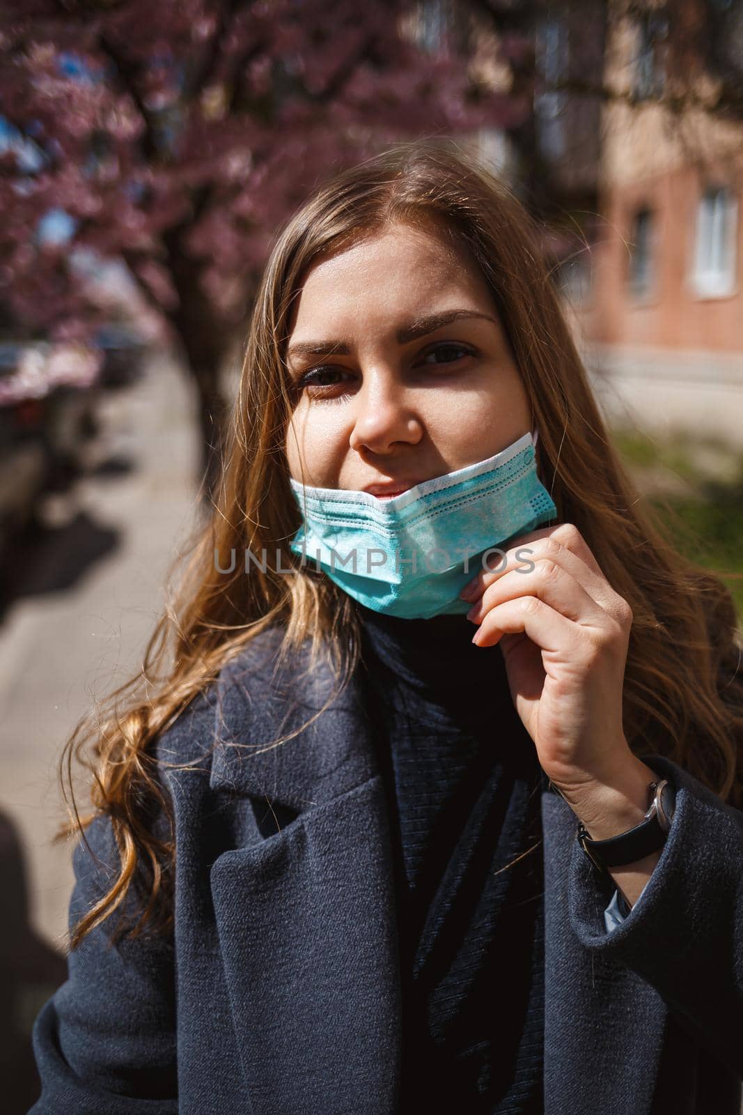 Girl, young woman in a protective sterile medical mask on her face, looking at the camera outdoors, in the spring garden. Air pollution, virus, pandemic coronavirus concept.