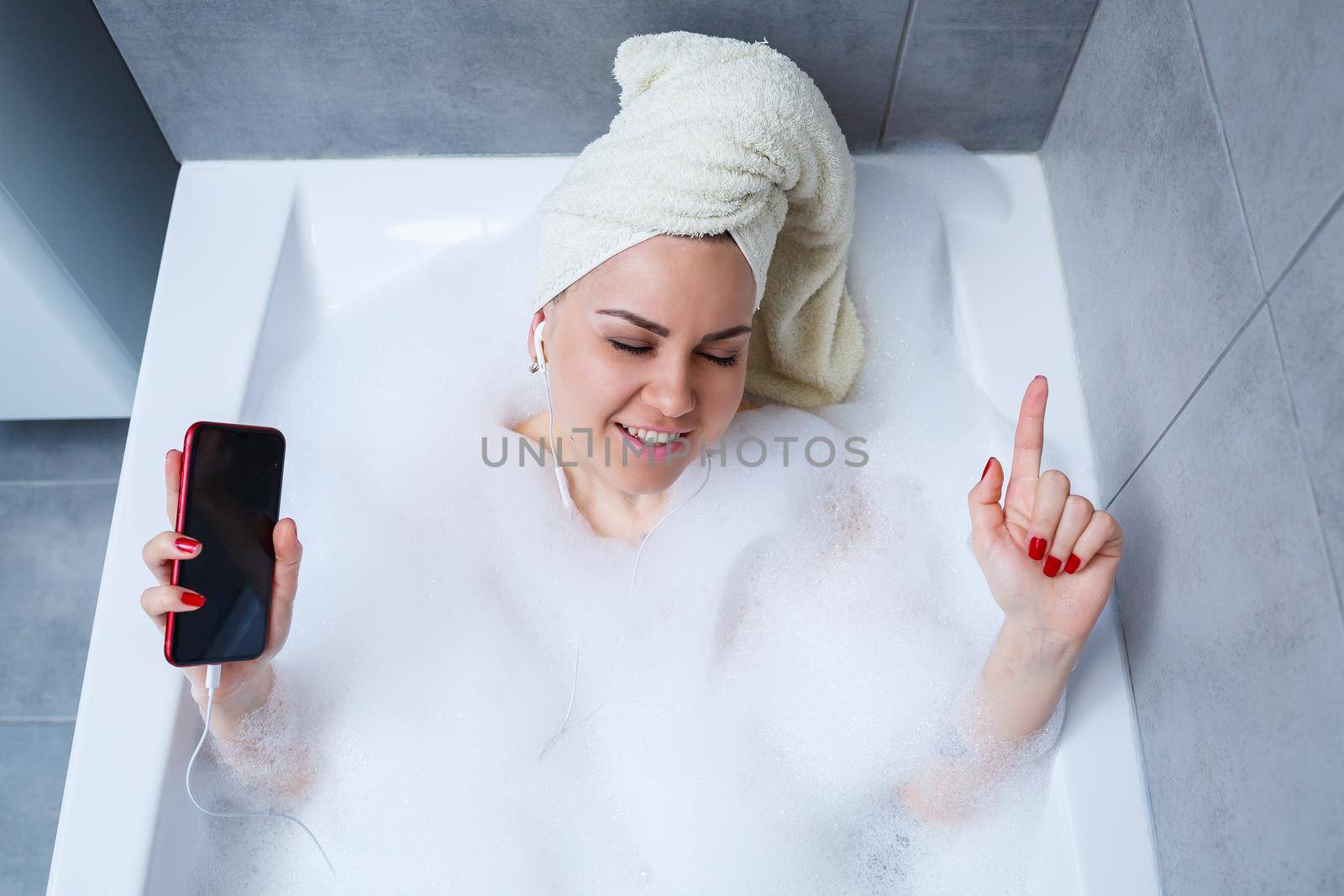 Beautiful young woman listening to music and singing while taking a bath at home. Relax after a hard day. Spa relaxing procedure.