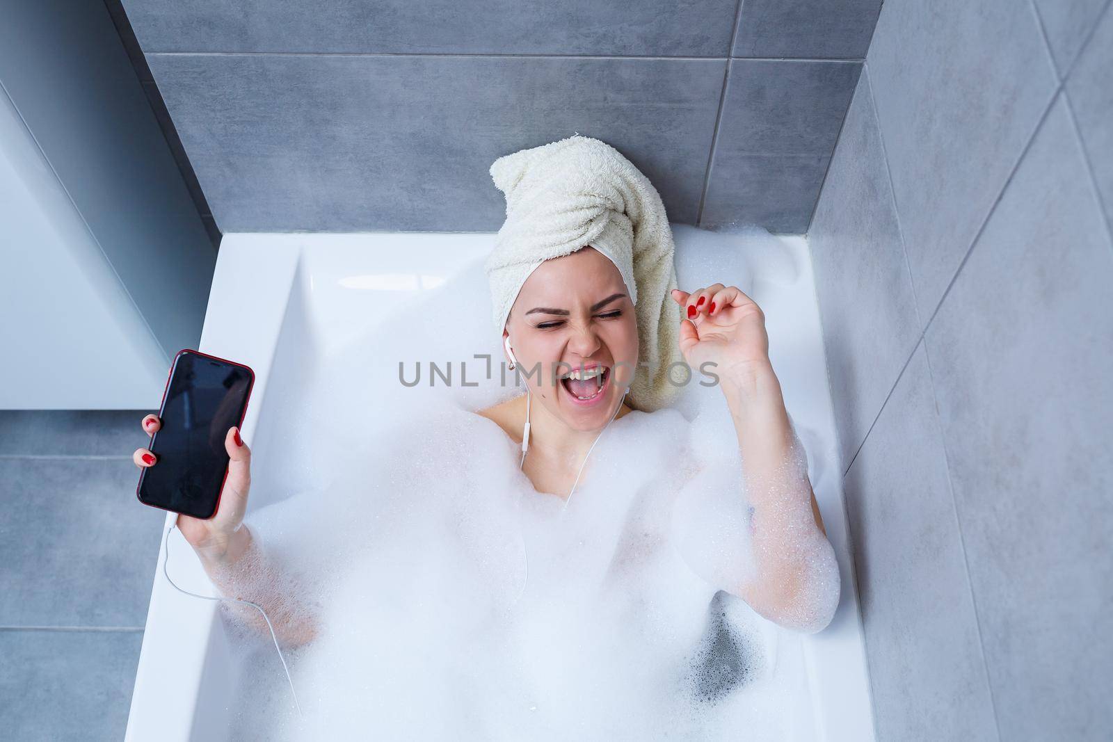 Beautiful young woman listening to music and singing while taking a bath at home. Relax after a hard day. Spa relaxing procedure.