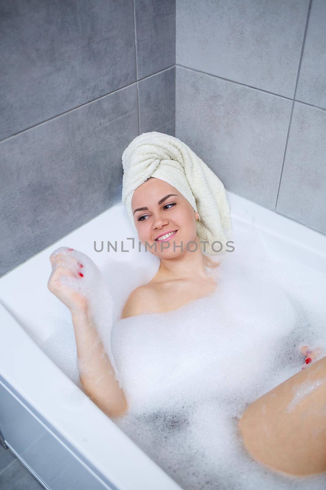 Girl woman with a white towel on her head lies in the bathroom in a white bath. Foam for around. Relax after a hard day. Spa relaxing treatment