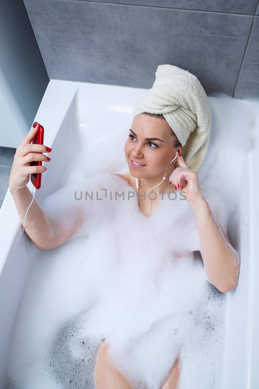 Beautiful young woman listening to music and singing while taking a bath at home. Relax after a hard day. Spa relaxing procedure.