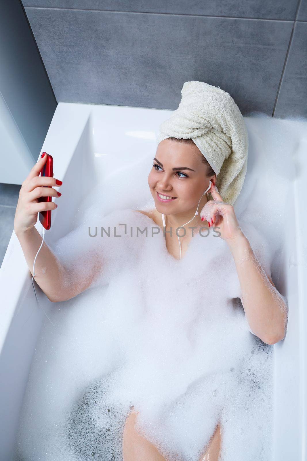 Beautiful young woman listening to music and singing while taking a bath at home. Relax after a hard day. Spa relaxing procedure.