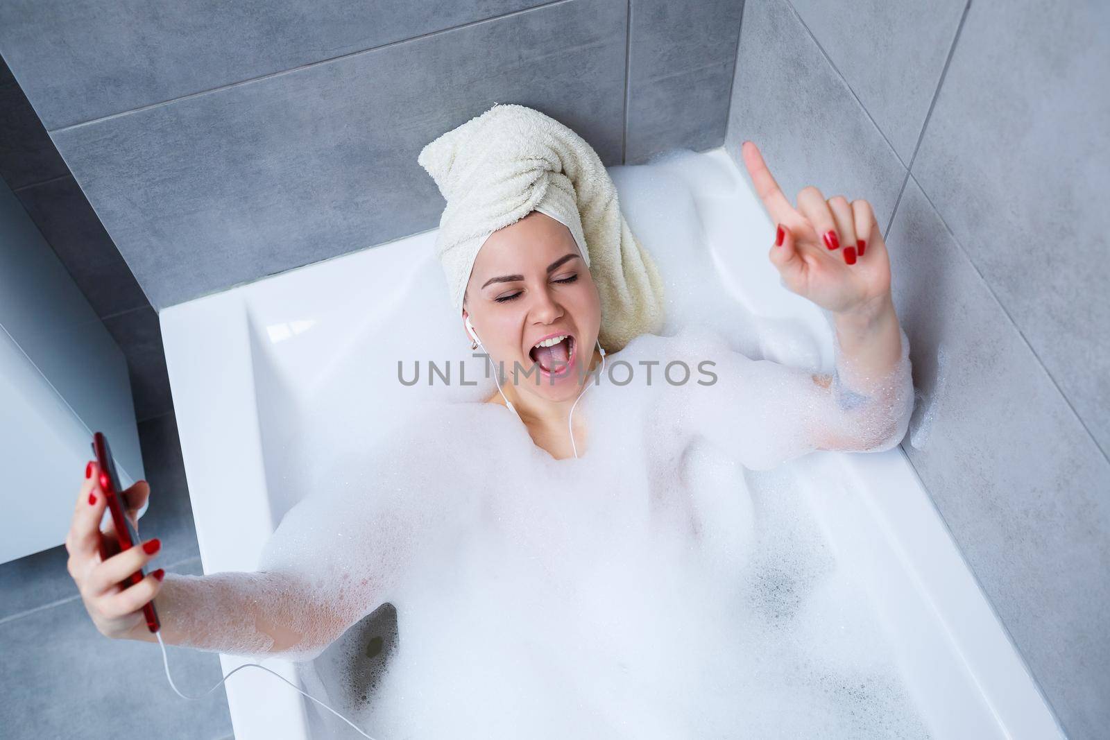 Beautiful young woman listening to music and singing while taking a bath at home. Relax after a hard day. Spa relaxing procedure.