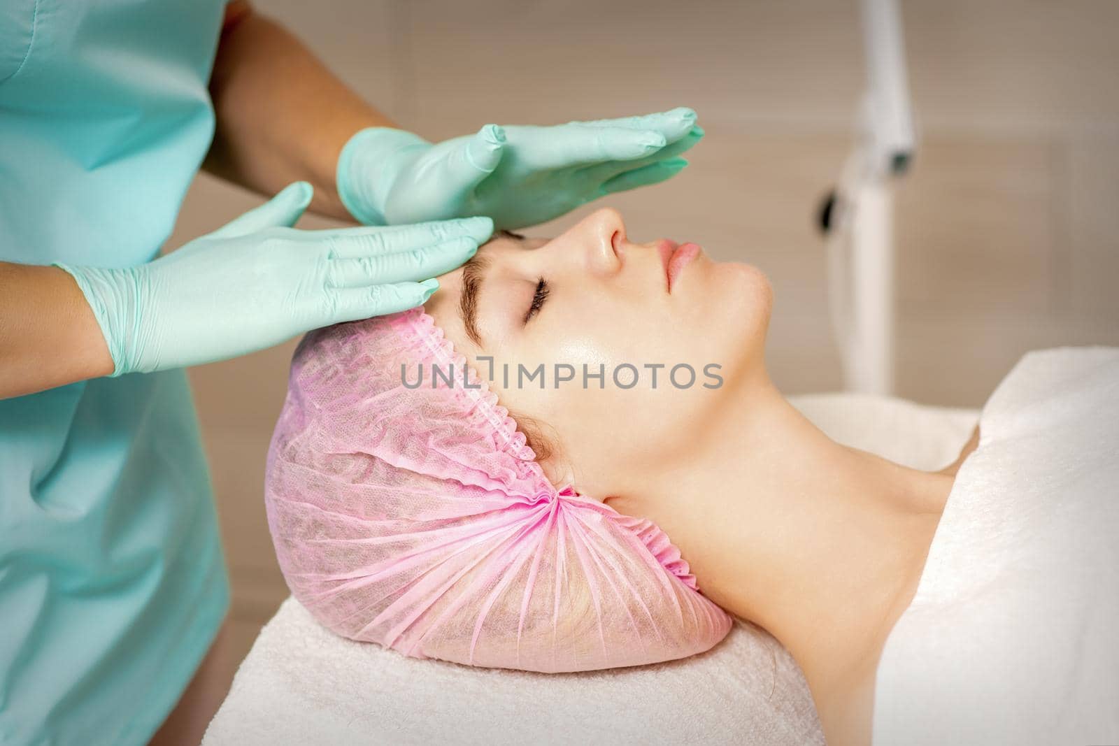 The woman is having cosmetic treatment during cosmetologist in medical gloves are touching the female face at the spa salon