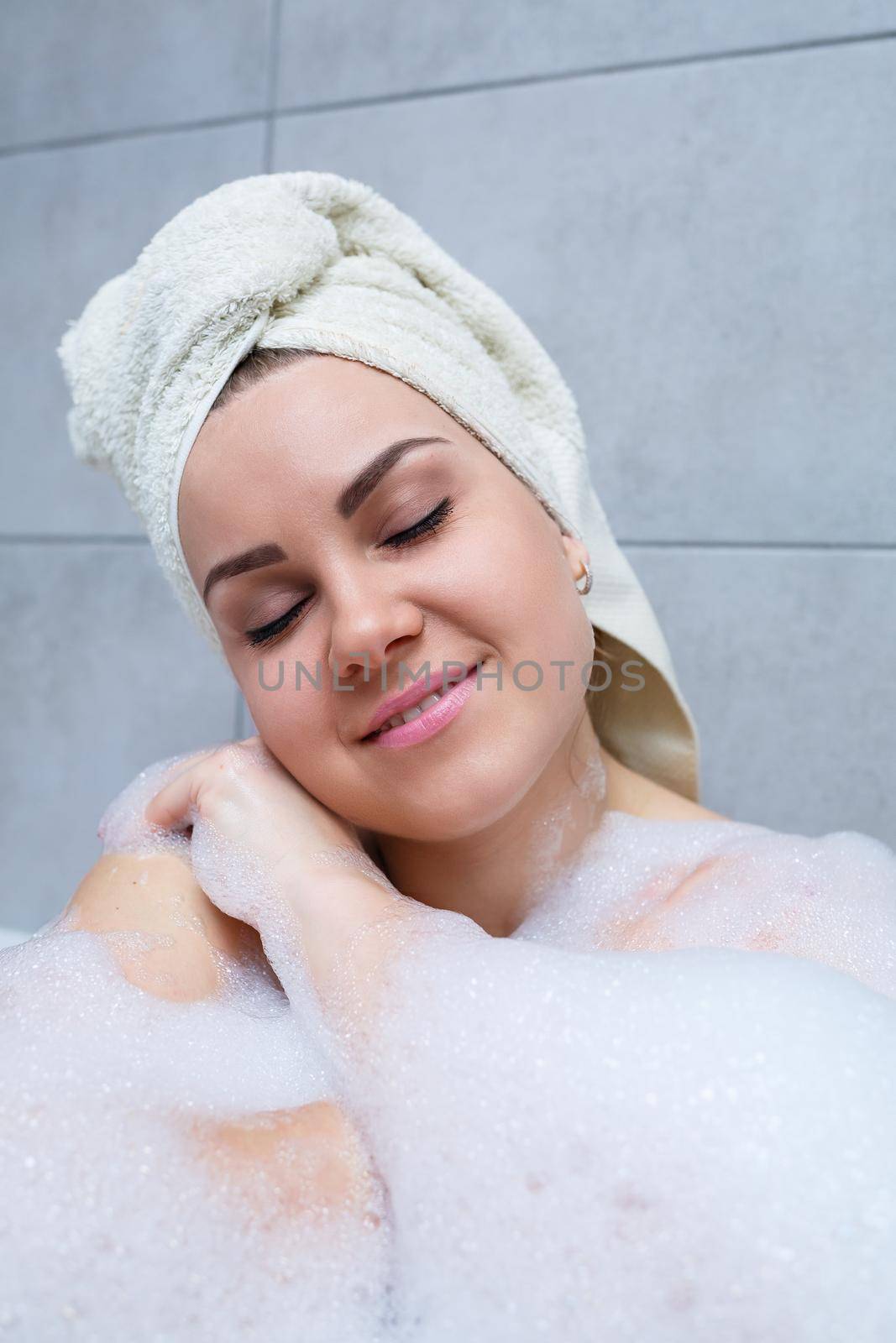Girl woman with a white towel on her head lies in the bathroom in a white bath. Foam for around. Relax after a hard day. Spa relaxing treatment