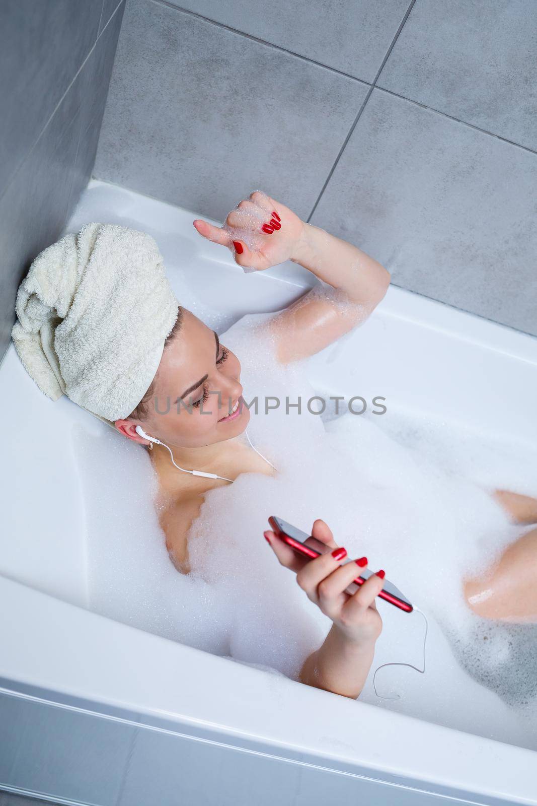 Beautiful young woman listens to music with headphones and sings while taking a bath at home. Relax after a hard day. Relaxing spa treatment.