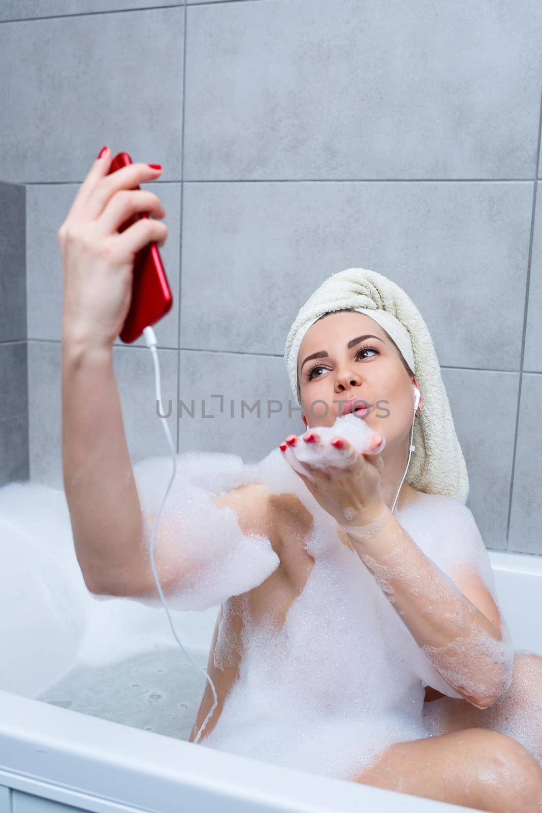 Beautiful young woman listens to music with headphones and sings while taking a bath at home. Relax after a hard day. Relaxing spa treatment.