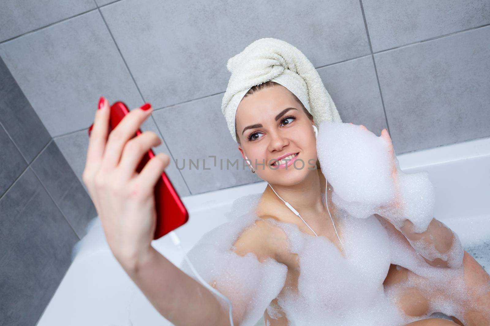 Beautiful young woman listening to music and singing while taking a bath at home. Relax after a hard day. Spa relaxing procedure.