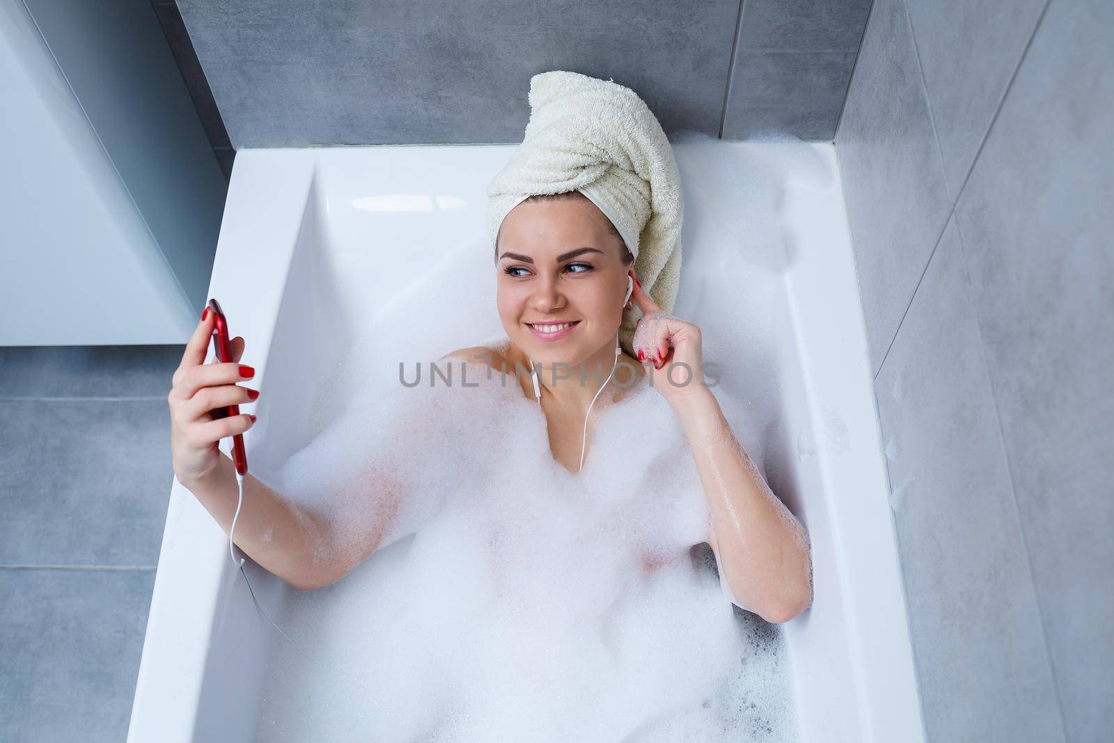Beautiful young woman listening to music and singing while taking a bath at home. Relax after a hard day. Spa relaxing procedure.