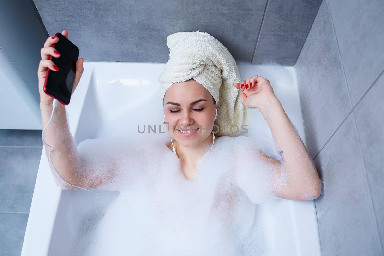 Beautiful young woman listening to music and singing while taking a bath at home. Relax after a hard day. Spa relaxing procedure.