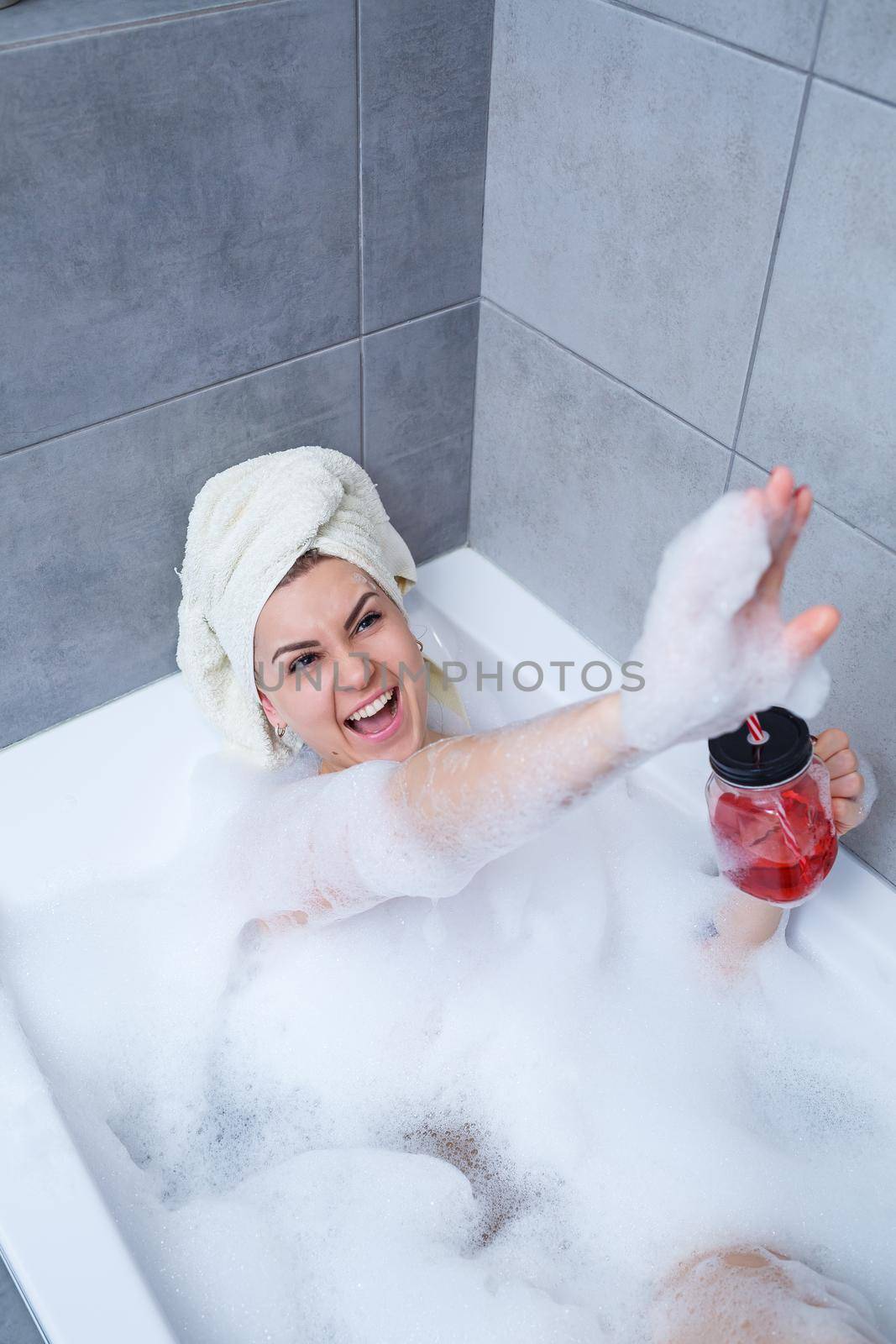 Beautiful young woman with a towel on her head drinking a cocktail takes a bath at home. Relax after a hard day. The spa is a relaxing procedure.