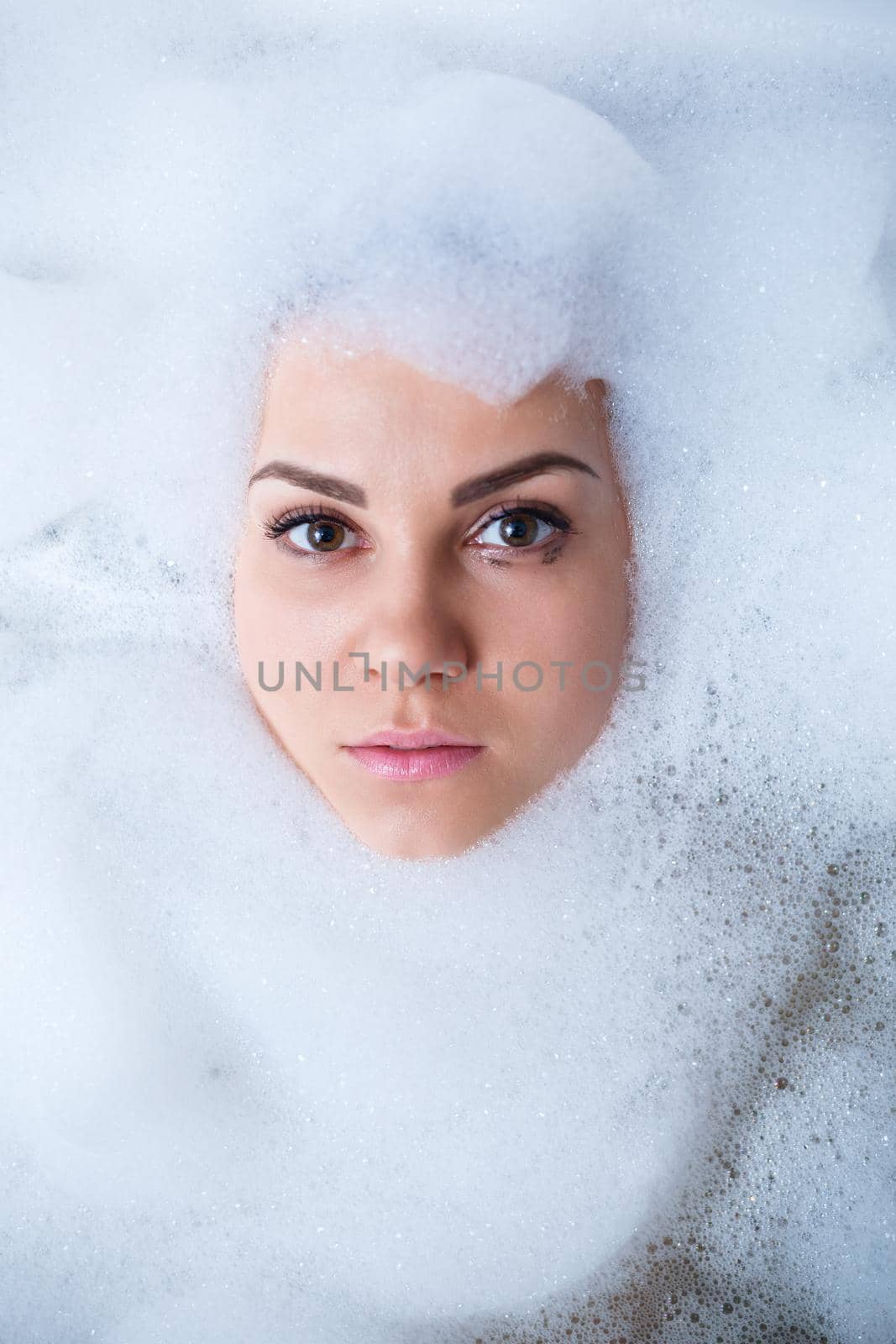 Closeup portrait of a girl in a bathtub and white foam around her face. Different emotions, grimaces, woman smile