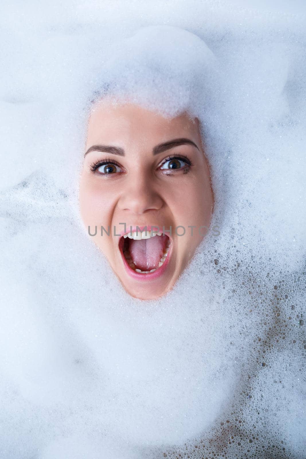 Closeup portrait of a girl in a bathtub and white foam around her face. Different emotions, grimaces, woman smile