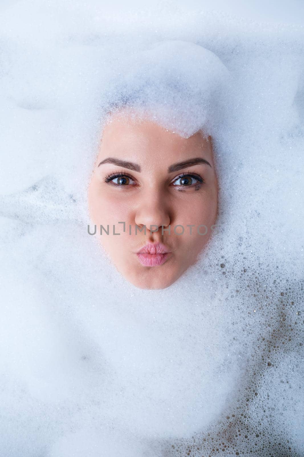 Closeup portrait of a girl in a bathtub and white foam around her face. Different emotions, grimaces, woman smile
