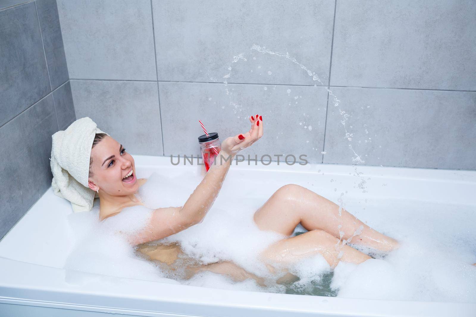 Beautiful young woman with a towel on her head drinking a cocktail takes a bath at home. Relax after a hard day. The spa is a relaxing procedure.