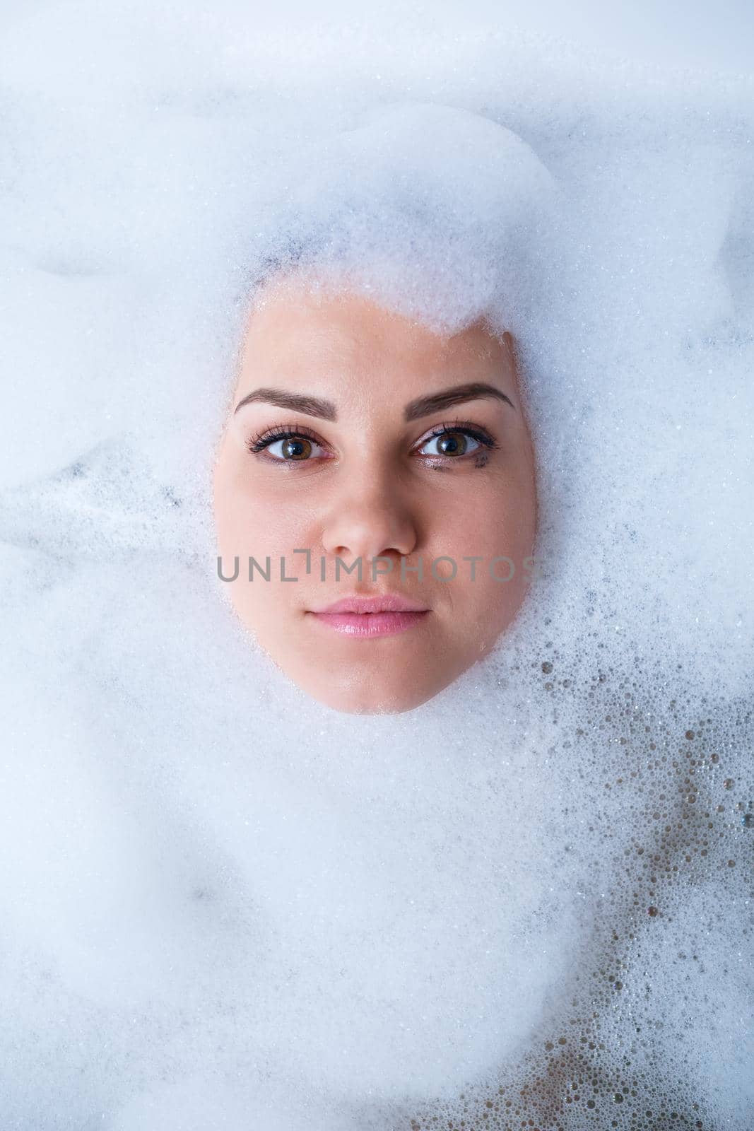 Closeup portrait of a girl in a bathtub and white foam around her face. Different emotions, grimaces, woman smile