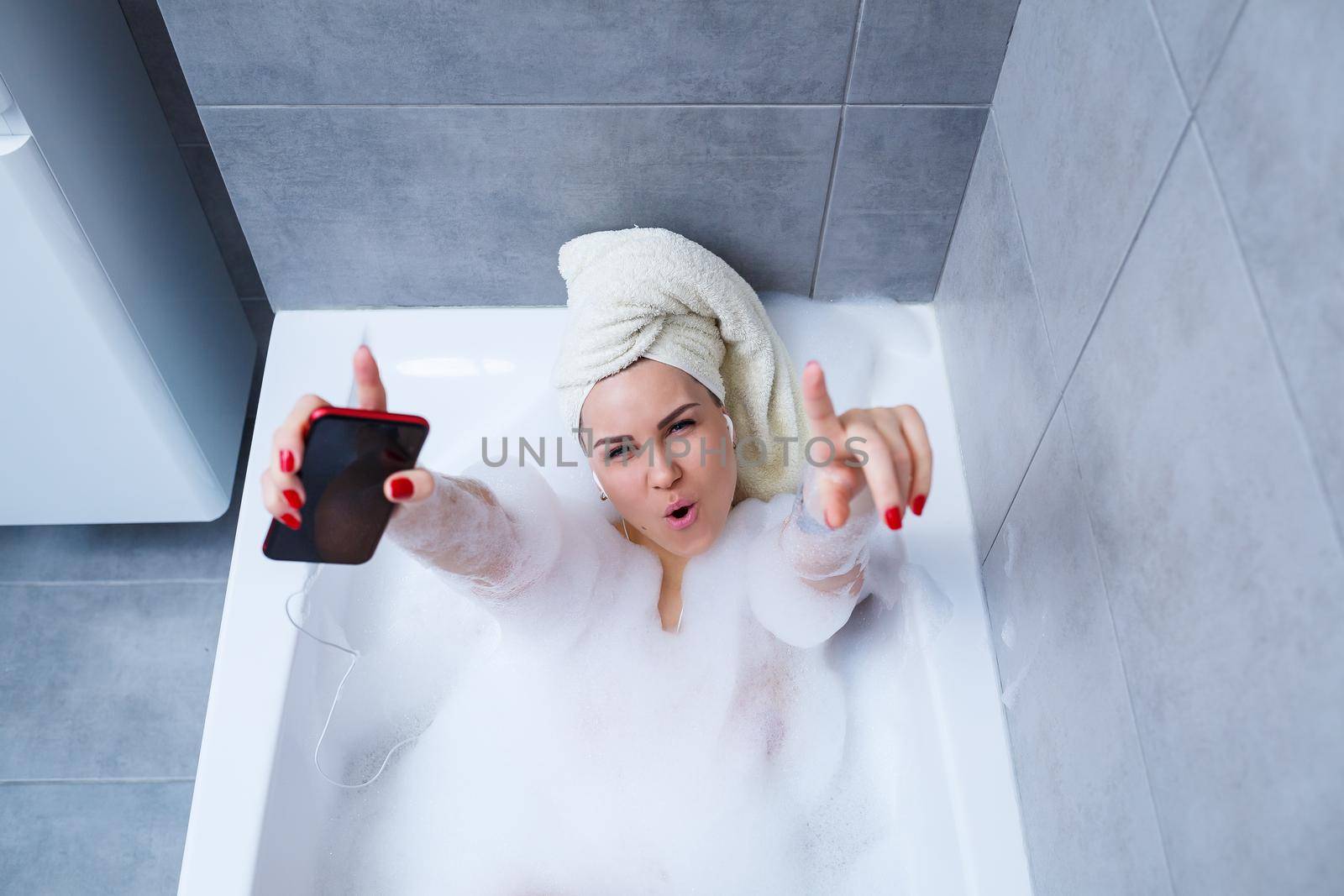 Beautiful young woman listening to music and singing while taking a bath at home. Relax after a hard day. Spa relaxing procedure.