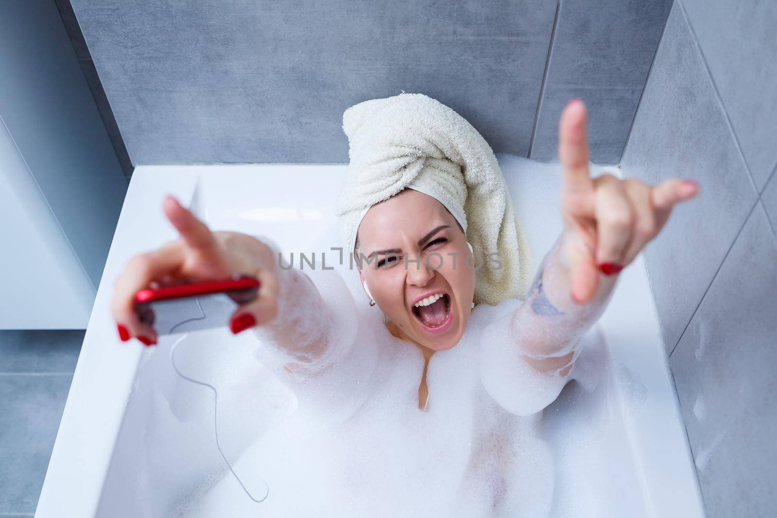 Beautiful young woman listening to music and singing while taking a bath at home. Relax after a hard day. Spa relaxing procedure.