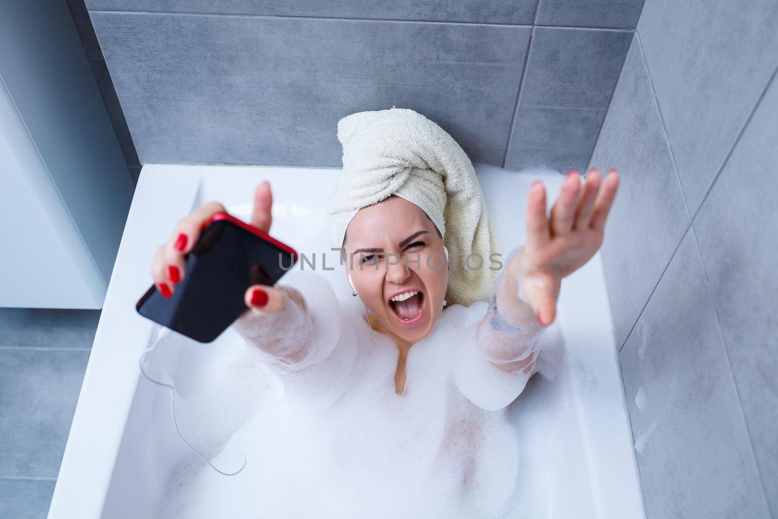 Beautiful young woman listening to music and singing while taking a bath at home. Relax after a hard day. Spa relaxing procedure.