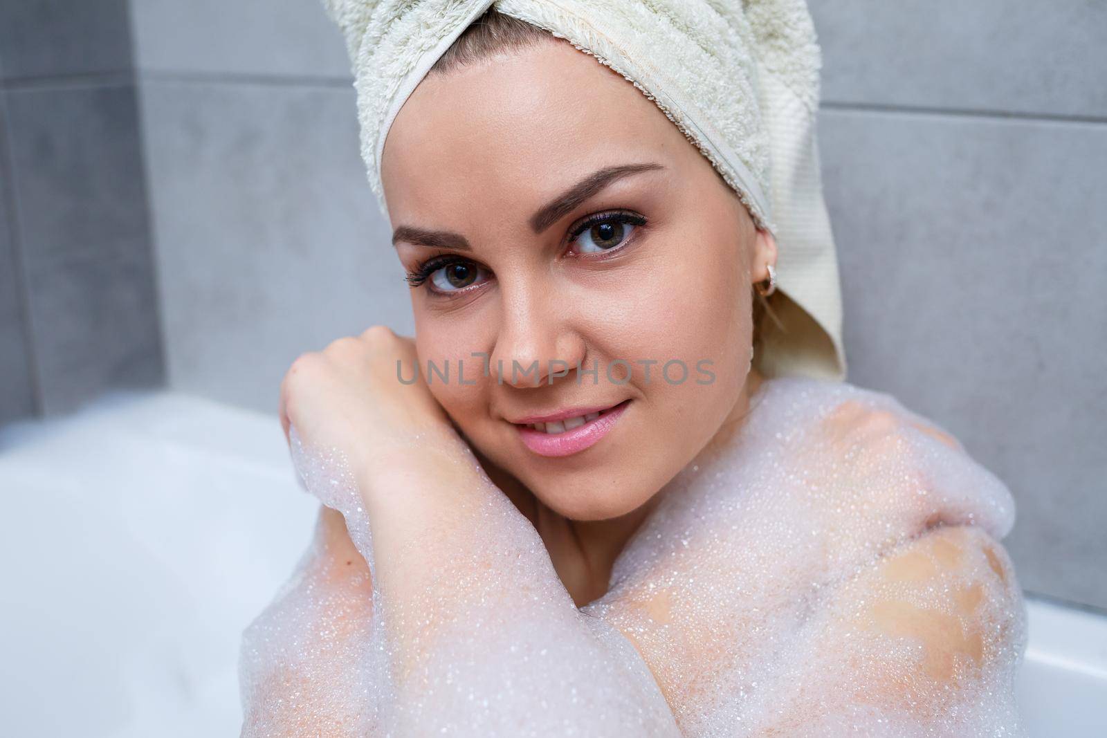 Girl woman with a white towel on her head lies in the bathroom in a white bath. Foam for around. Relax after a hard day. Spa relaxing treatment