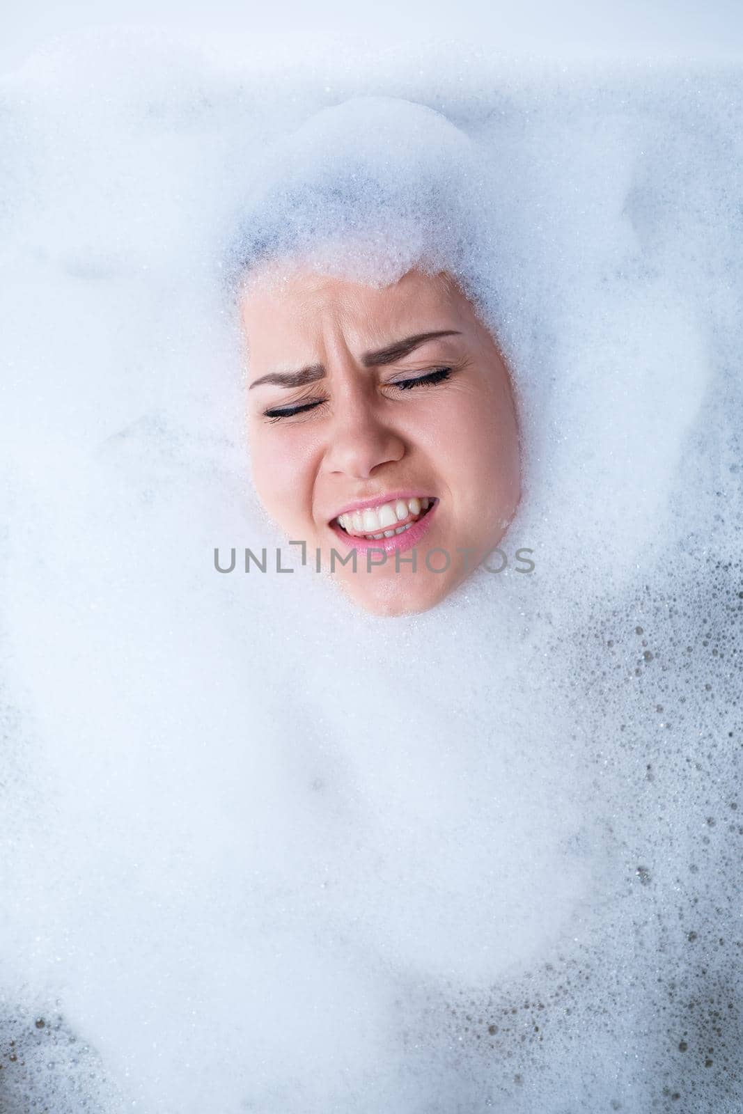 Closeup portrait of a girl in a bathtub and white foam around her face. Different emotions, grimaces, woman smile
