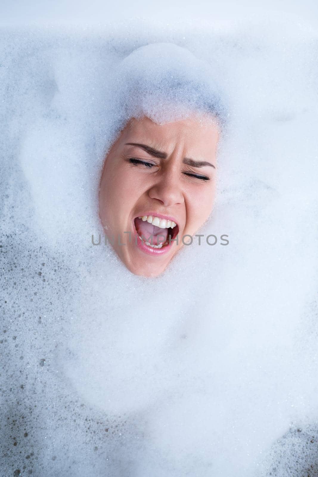 Closeup portrait of a girl in a bathtub and white foam around her face. Different emotions, grimaces, woman smile