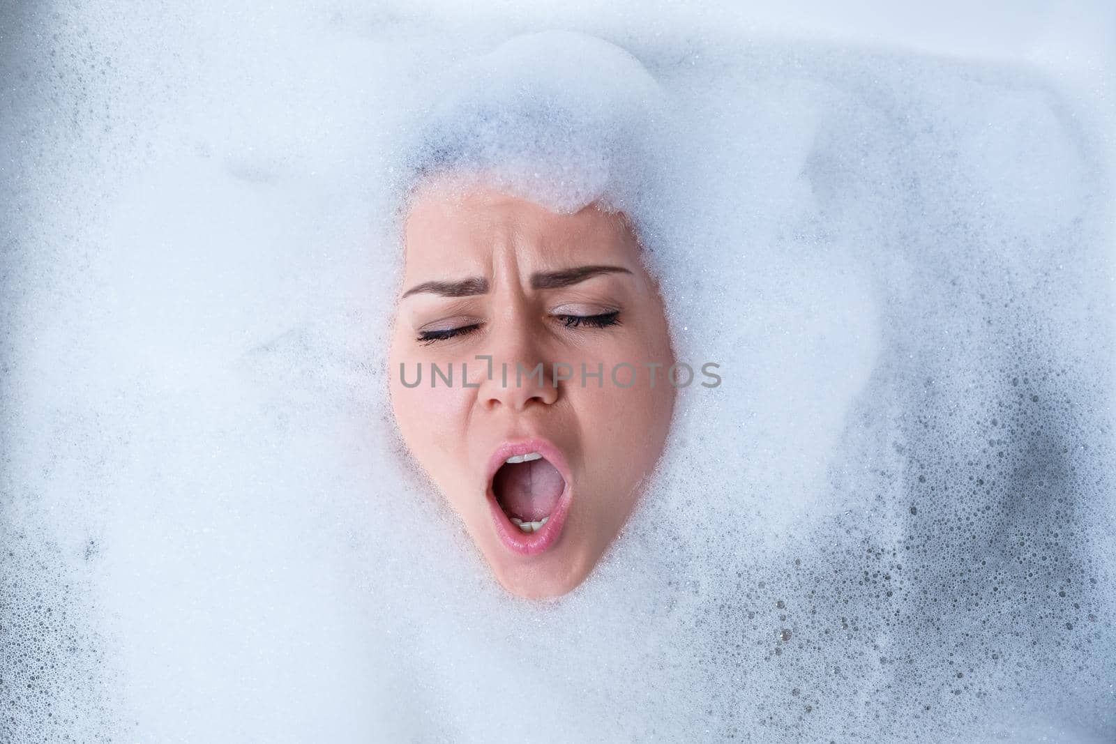 Closeup portrait of a girl in a bathtub and white foam around her face. Different emotions, grimaces, woman smile