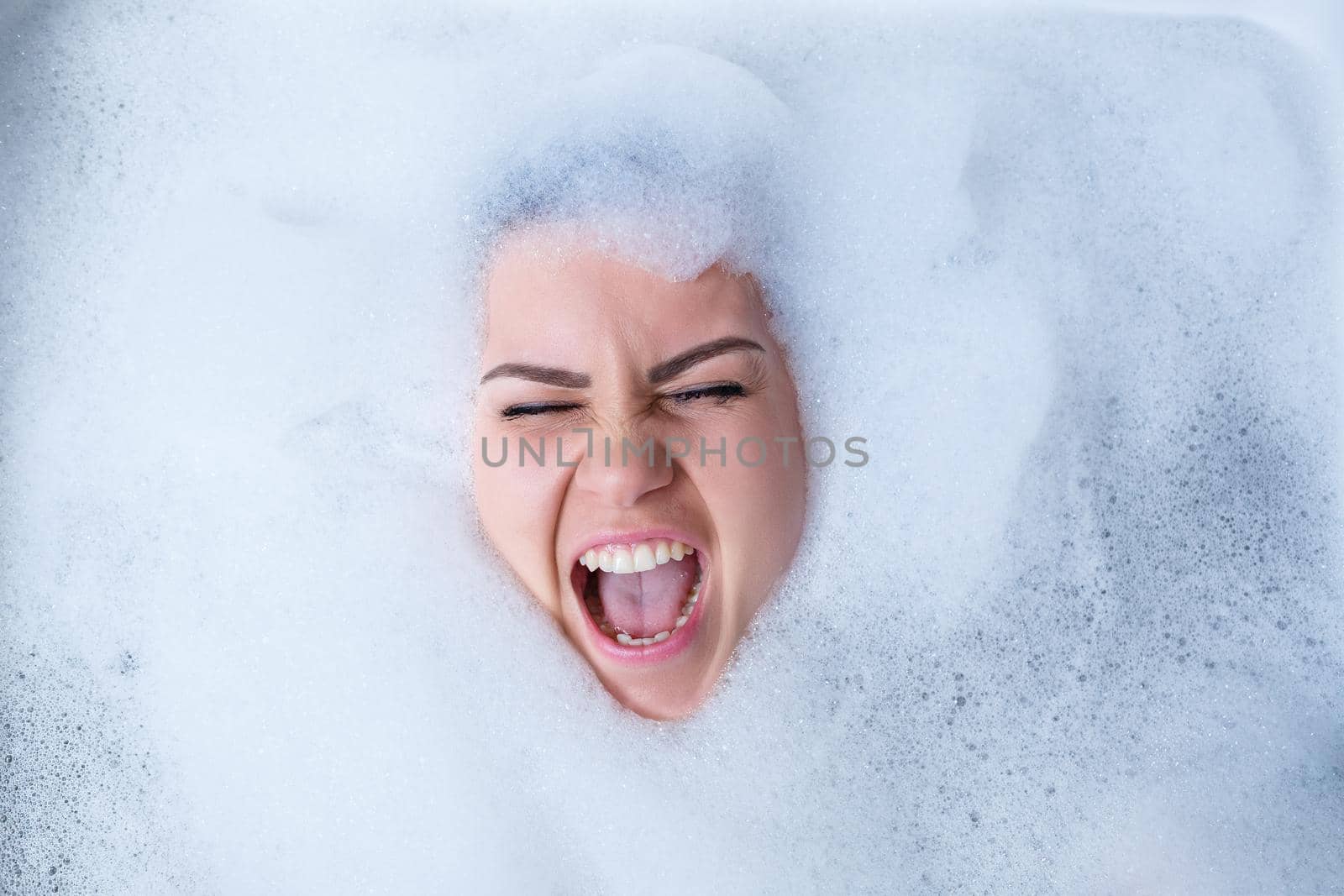 Closeup portrait of a girl in a bathtub and white foam around her face. Different emotions, grimaces, woman smile