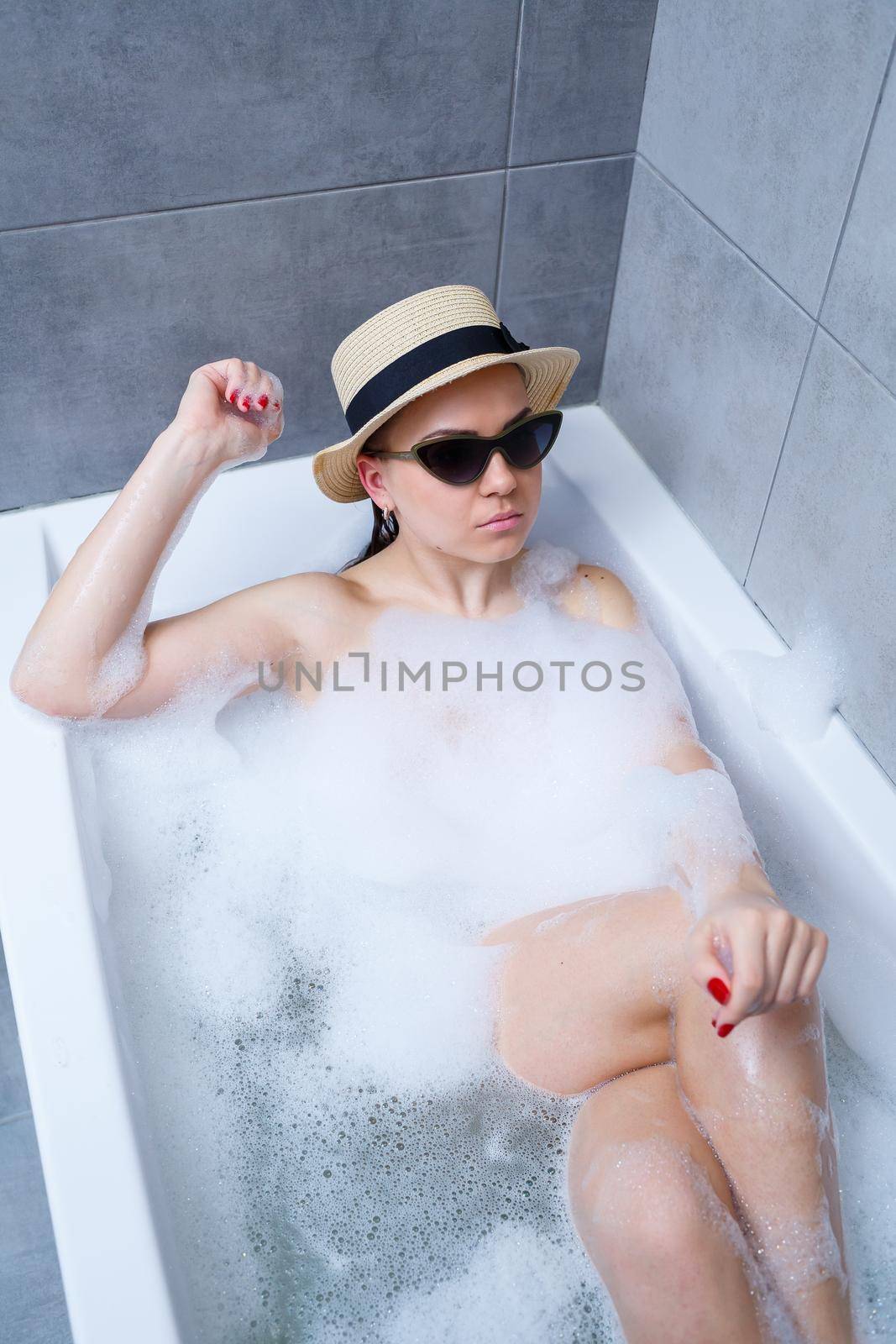 Young woman in a hat and sunglasses takes a bath at home. Relax after a hard day. The spa is a relaxing procedure.