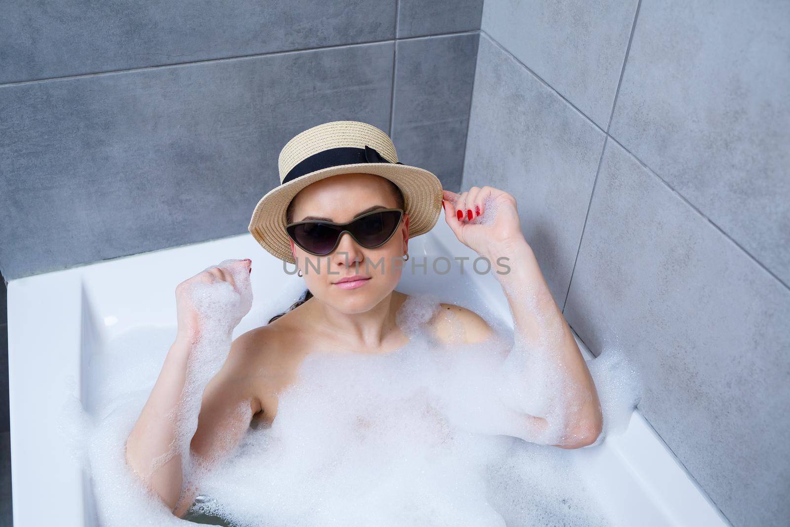Young woman in a hat and sunglasses takes a bath at home. Relax after a hard day. The spa is a relaxing procedure.