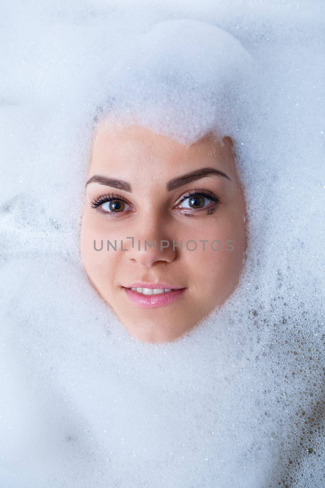 Closeup portrait of a girl in a bathtub and white foam around her face. Different emotions, grimaces, woman smile