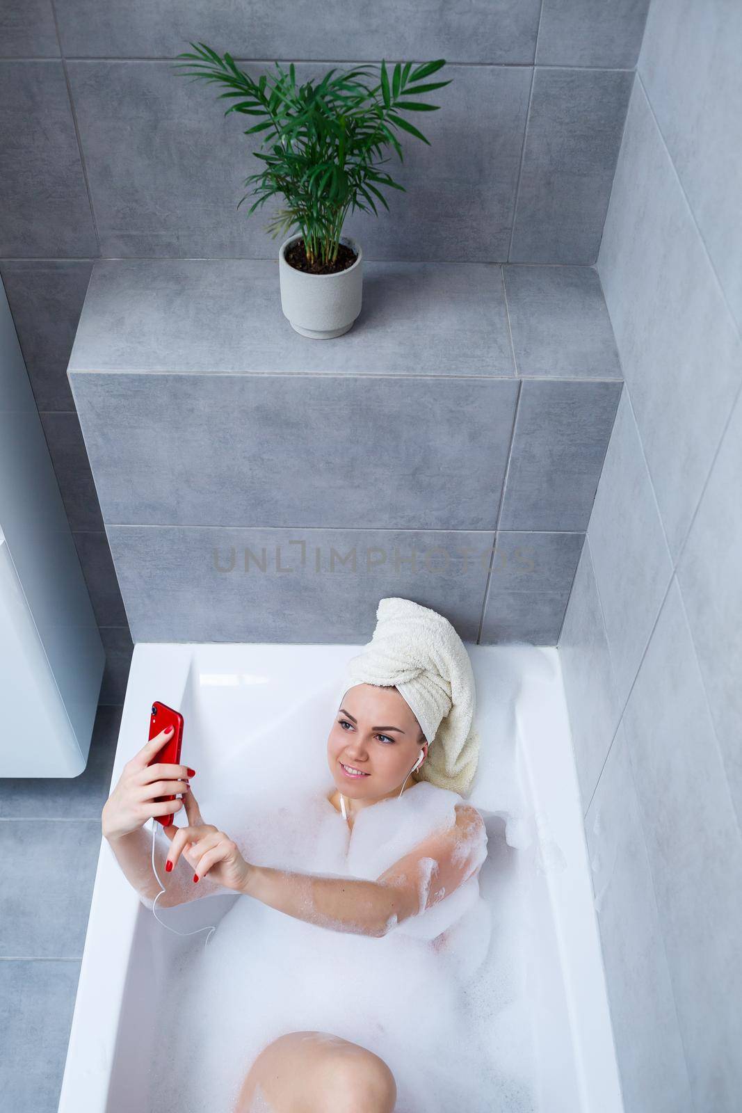 Beautiful young woman listening to music and singing while taking a bath at home. Relax after a hard day. Spa relaxing procedure.