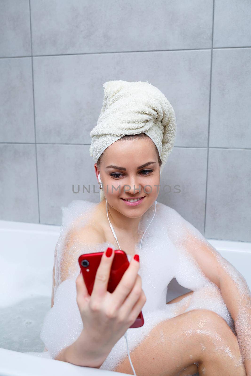 Beautiful young woman listens to music with headphones and sings while taking a bath at home. Relax after a hard day. Relaxing spa treatment.