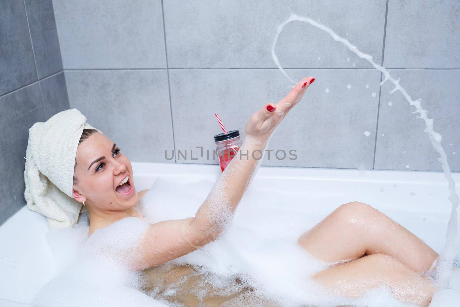 Beautiful young woman with a towel on her head drinking a cocktail takes a bath at home. Relax after a hard day. The spa is a relaxing procedure.