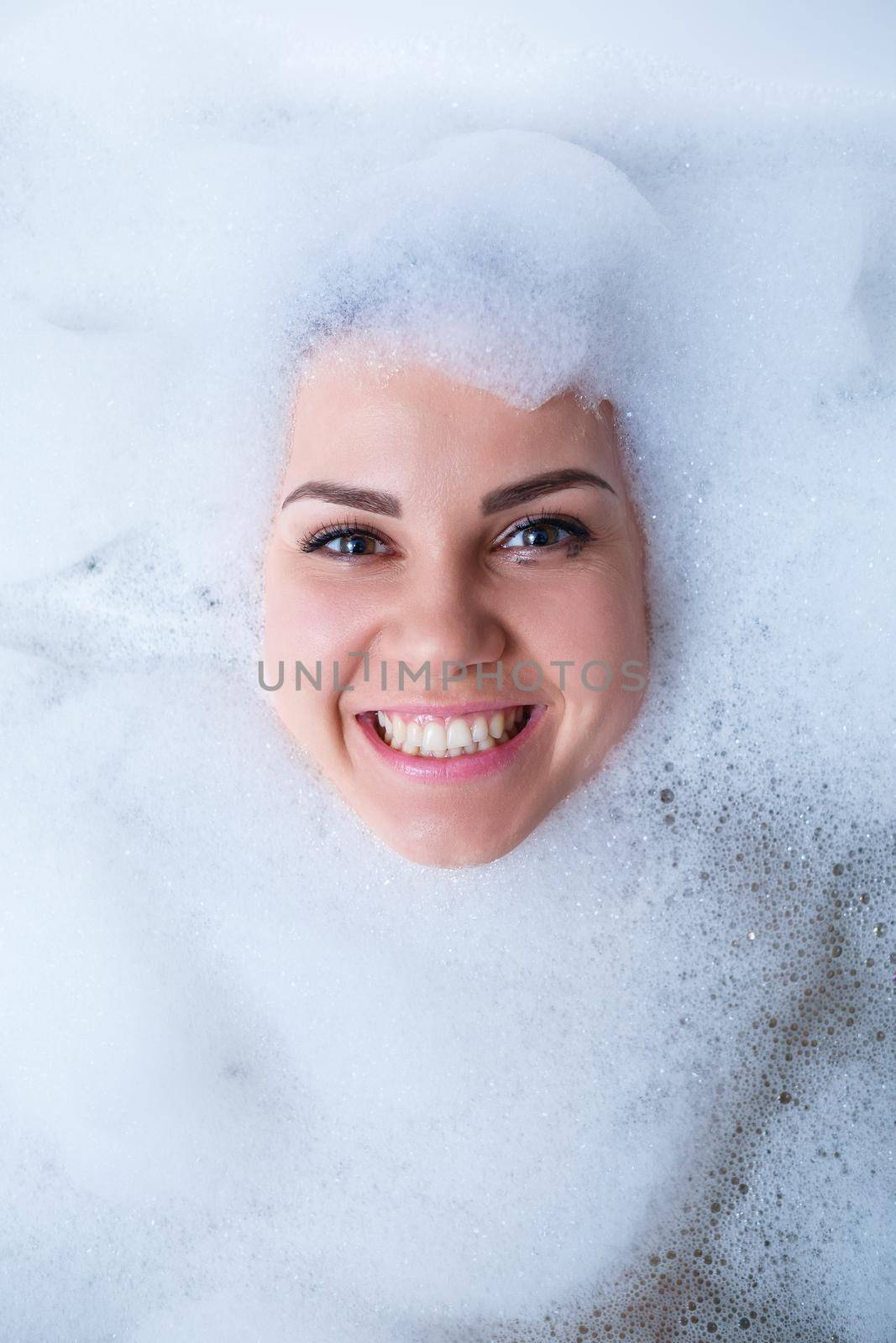 Closeup portrait of a girl in a bathtub and white foam around her face. Different emotions, grimaces, woman smile