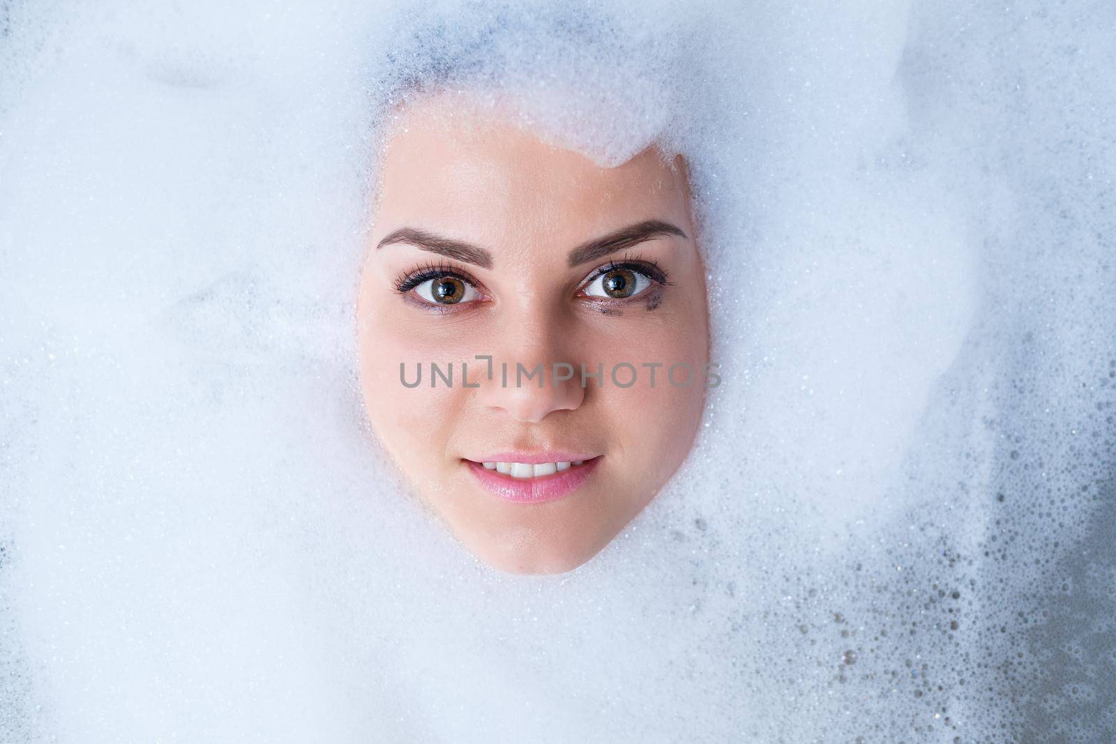 Closeup portrait of a girl in a bathtub and white foam around her face. Different emotions, grimaces, woman smile