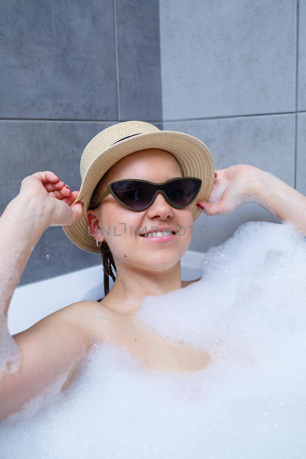Young woman in a hat and sunglasses takes a bath at home. Relax after a hard day. The spa is a relaxing procedure.