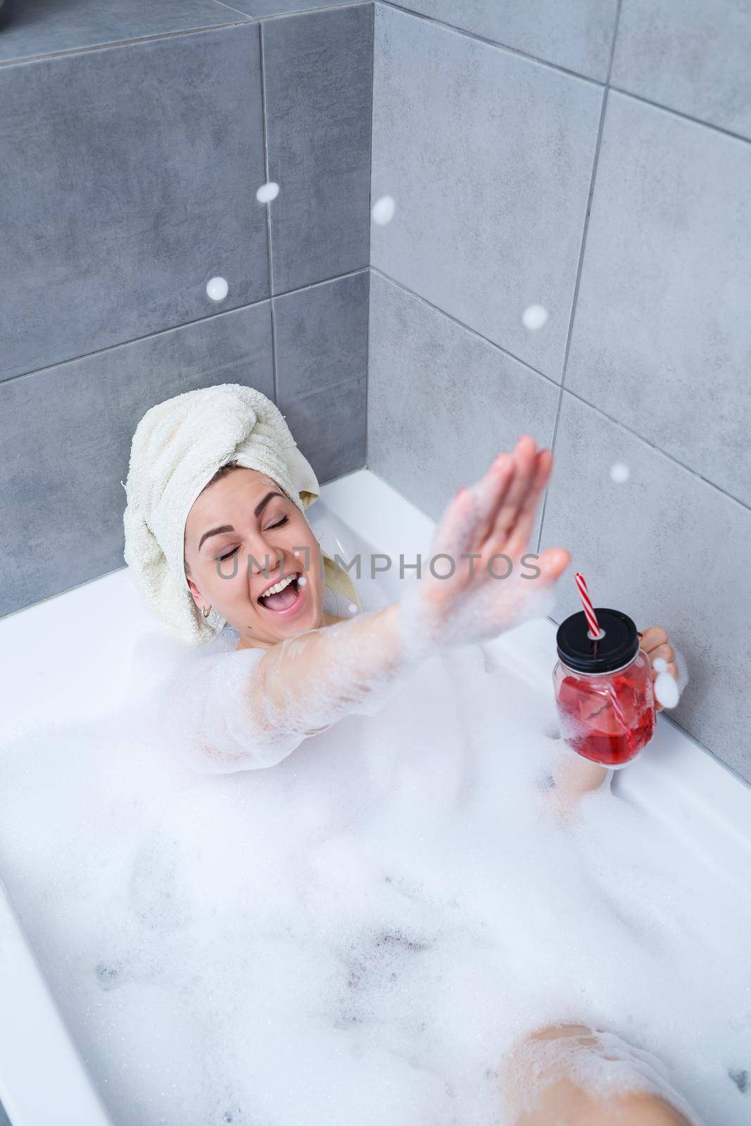 Beautiful young woman with a towel on her head, drinking a cocktail, takes a bath at home. Relax after a hard day.