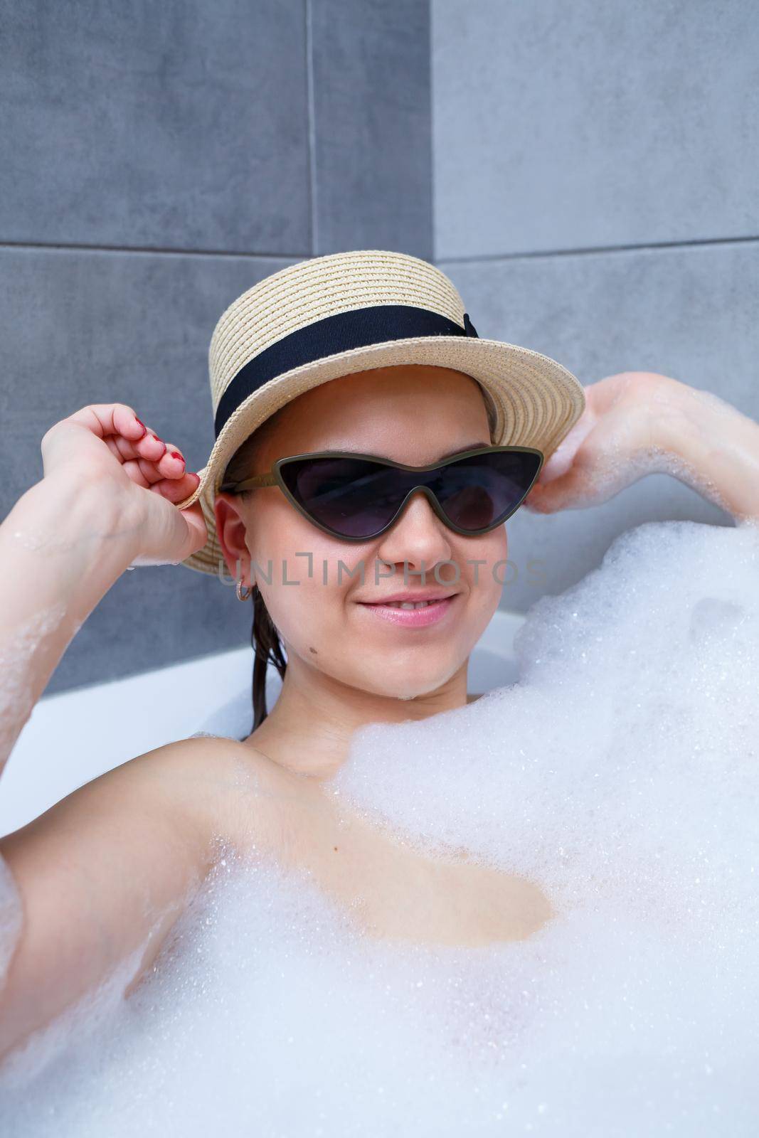 Young woman in a hat and sunglasses takes a bath at home. Relax after a hard day. The spa is a relaxing procedure.