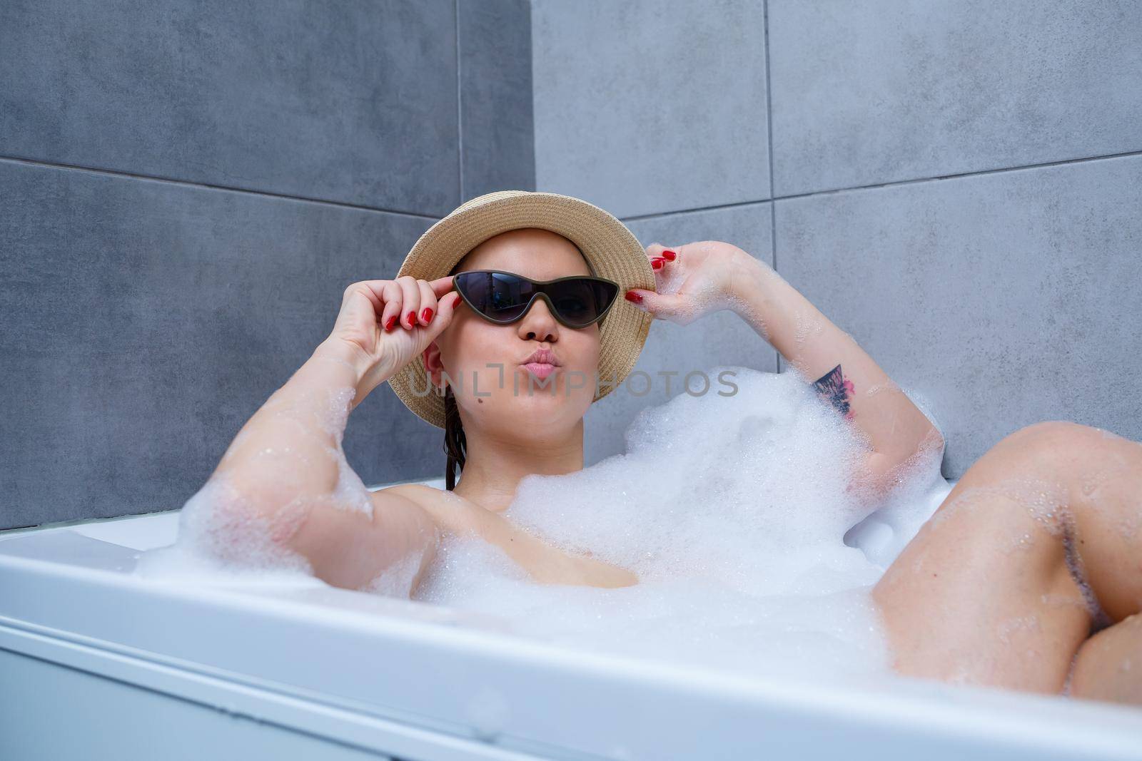 Young woman in a hat and sunglasses takes a bath at home. Relax after a hard day. The spa is a relaxing procedure.