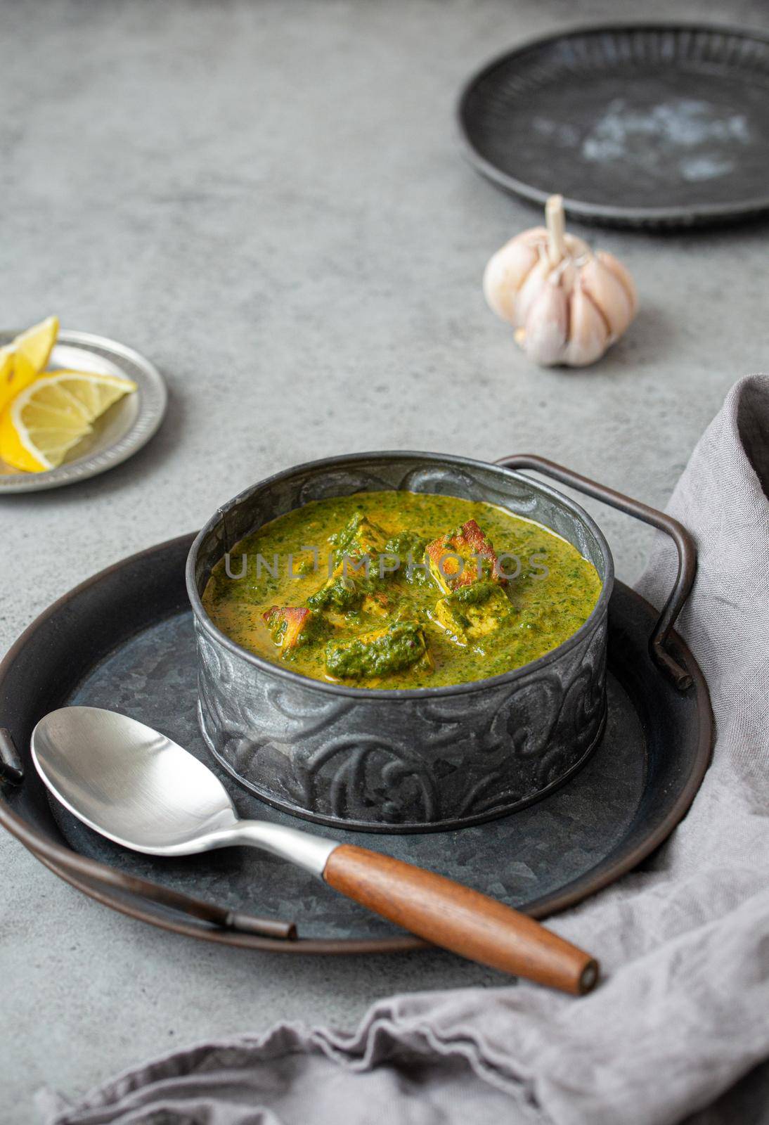 Traditional vegetarian Indian Punjabi food Palak Paneer with spinach and cheese in vintage metal bowl with spoon on rustic grey concrete background table, angle view