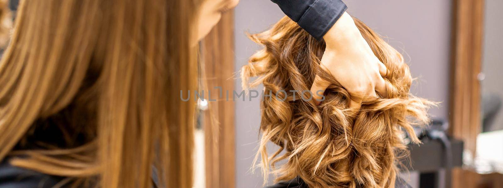 Female hairdresser checks brown curly hairstyle of a young caucasian woman in beauty salon