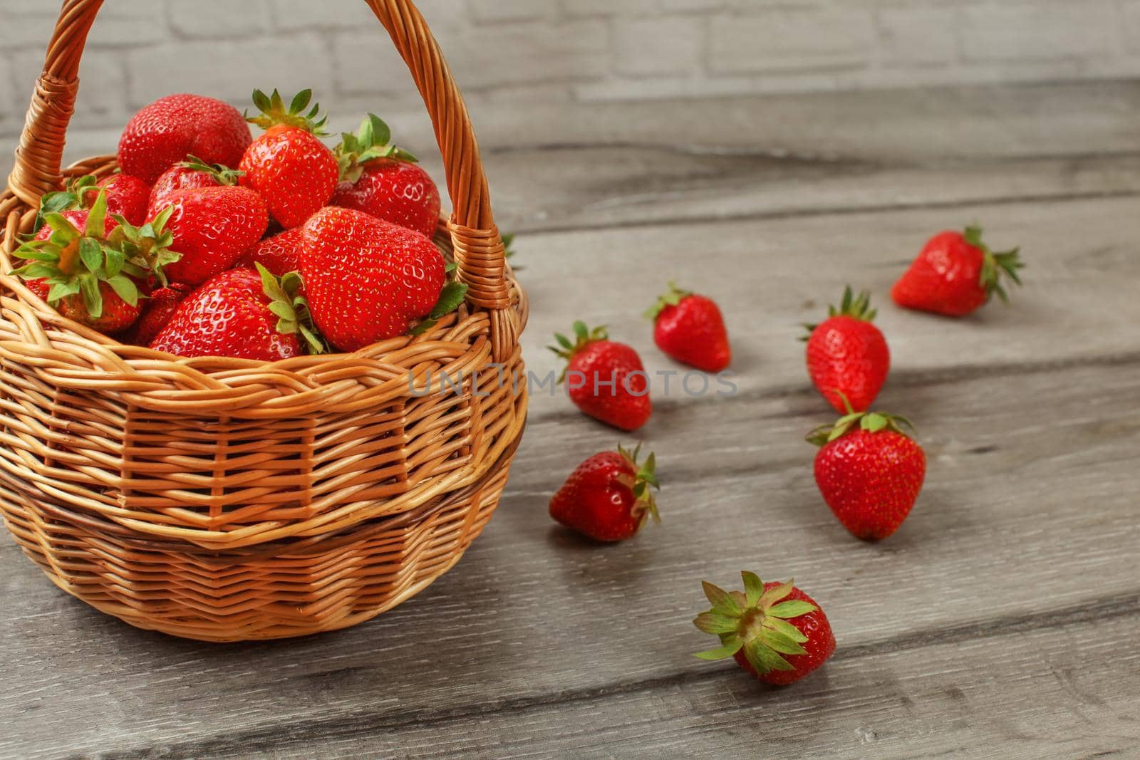 Basket with strawberries, some of them spilled on gray wood desk.