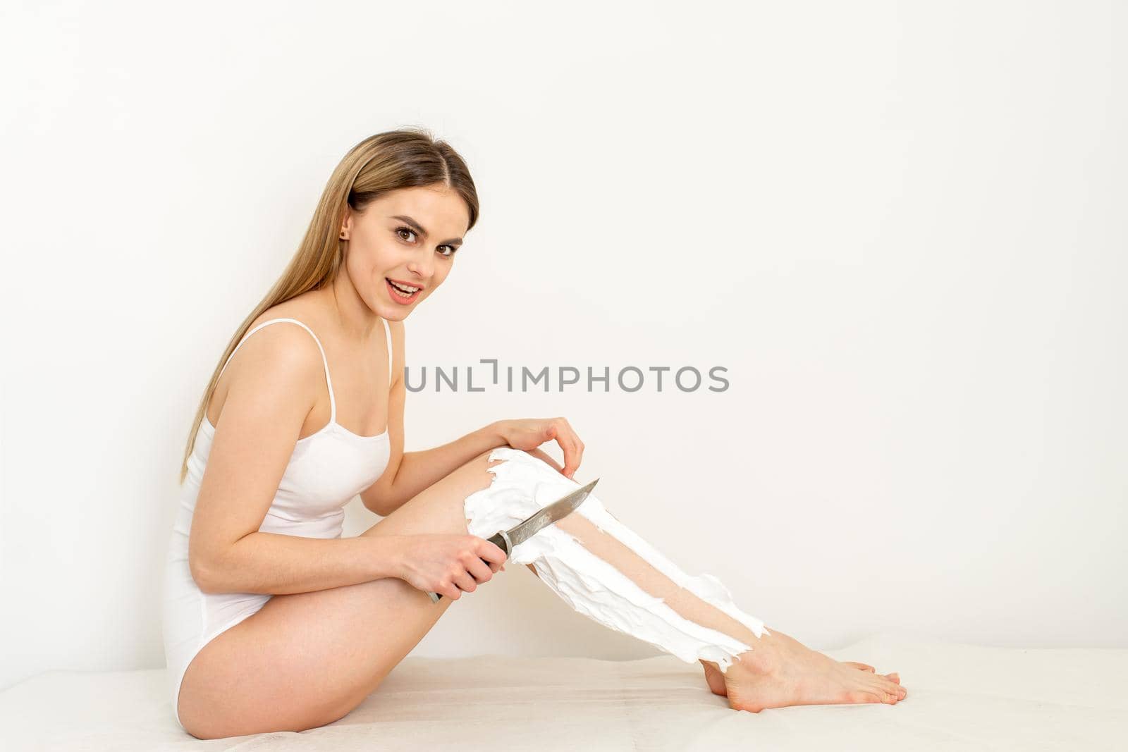 Beautiful caucasian woman shaving her legs with a knife with shaving foam on white background. Depilation and epilation concept
