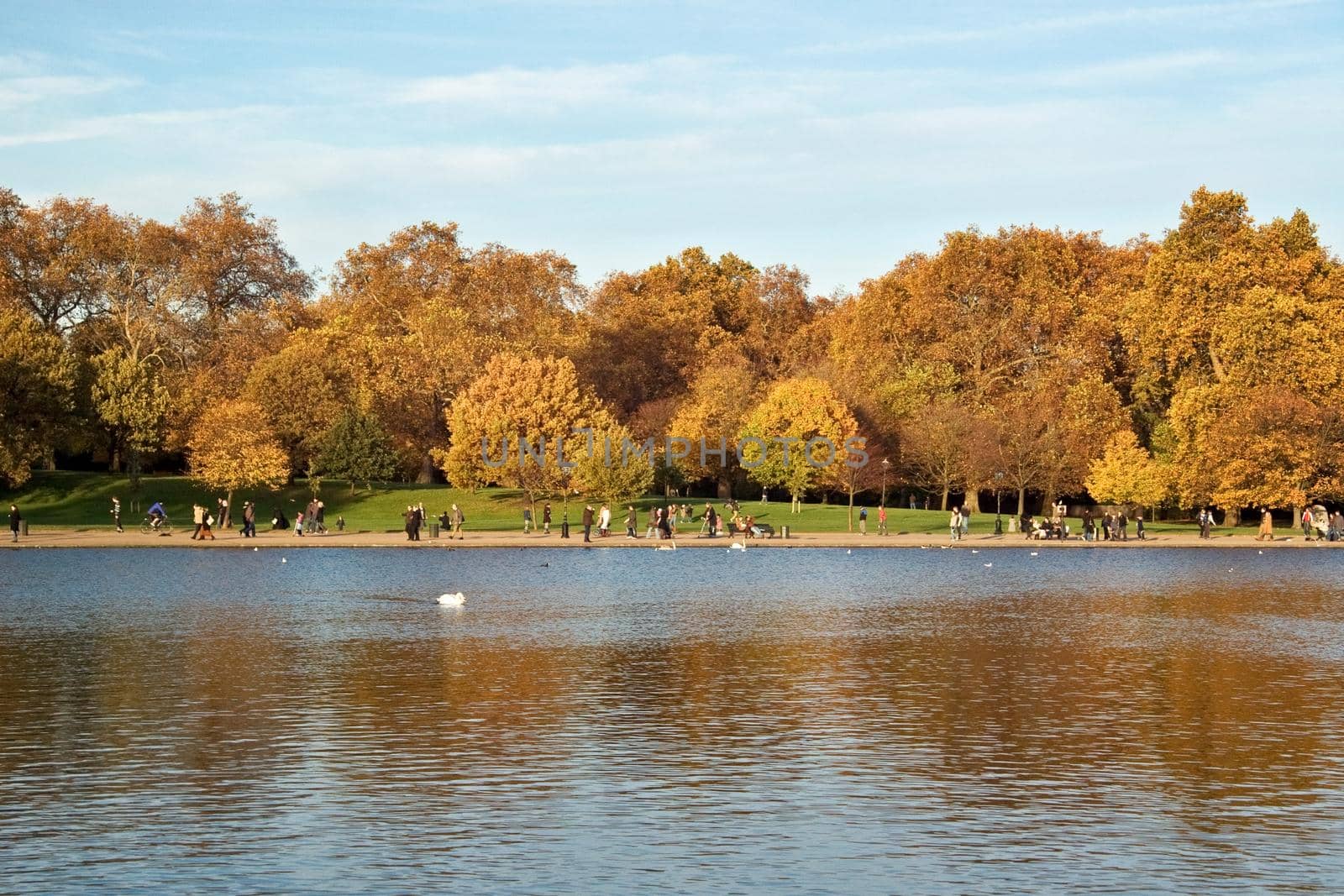 London, United Kingdom - November 19th, 2006: People enjoying sunny autumn afternoon in Hyde Park, walking on pavement near The Serpentine lake.